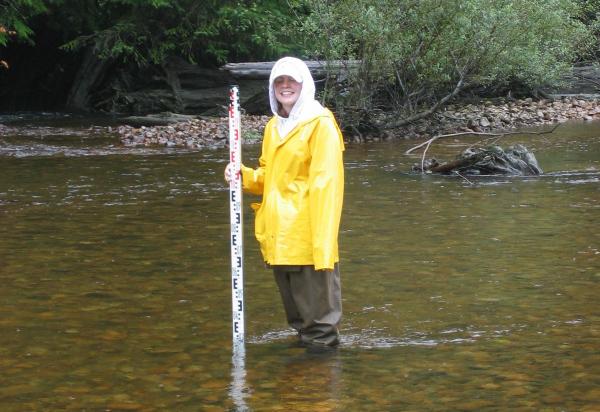 student in rain gear standing in water holding measuring stick