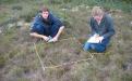 two students kneeling in field taking measurements
