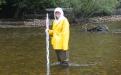 student in rain gear standing in water holding measuring stick